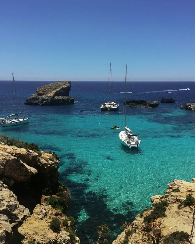 Boats anchored in clear turquoise water below rocky cliffs