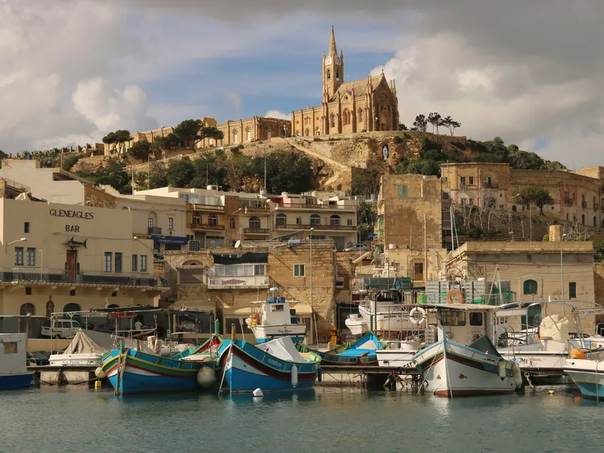 Painted fishing boats in a Maltese harbour below a hilltop church