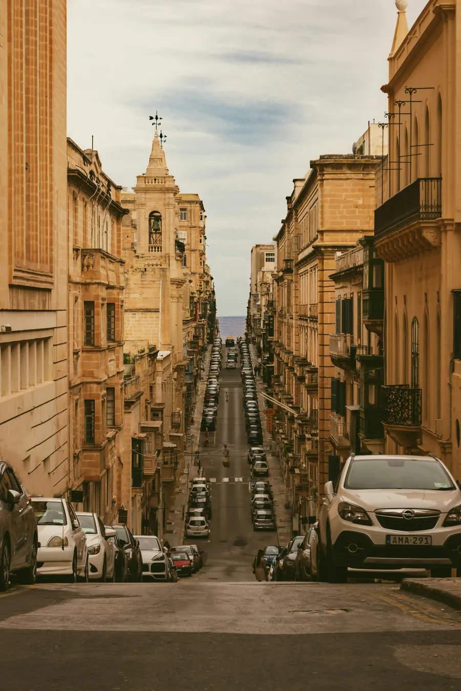 A narrow Valletta street running downhill between limestone buildings, framed like a vertical shot